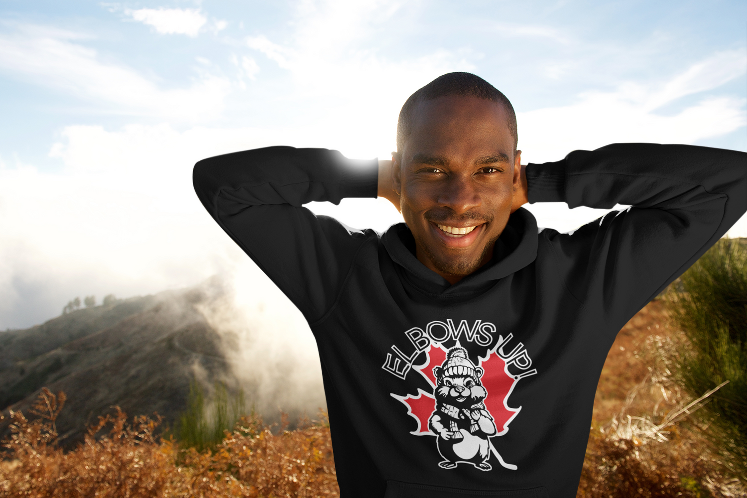 black man wearing a hooded sweatshirt with a graphic that says "elbows up" and contains the image of a maple leaf and beaver.